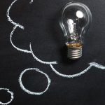 Light bulb laying on chalkboard with drawn thought bubble, symbolizing creative ideas.