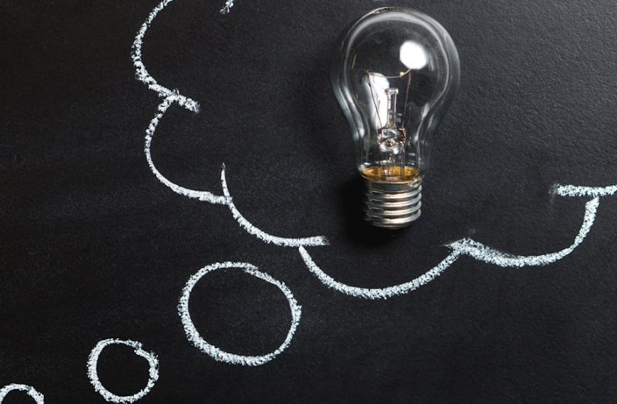 Light bulb laying on chalkboard with drawn thought bubble, symbolizing creative ideas.